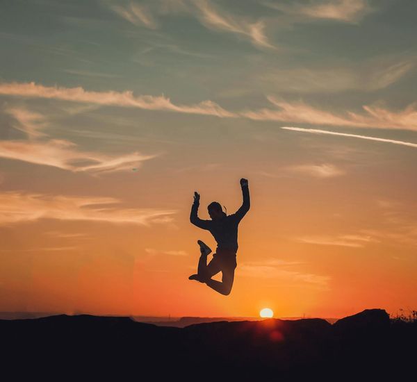 A person looking energetic and happy while stretching outdoors at sunrise.